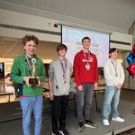 Top four winners on stage receiving medals and a trophy.